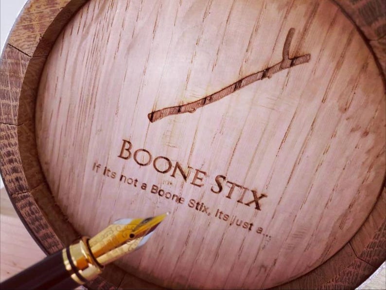 May include: Close-up of a wooden barrel lid with the text "BOONE STIX" and a branch design. A gold-tipped fountain pen is in the foreground. The text "If Its not a Boone Stix, Its just a..." is also visible.