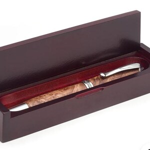 May include: A wooden pen set in a dark brown box with a hinged lid. The pen has a silver-colored clip and tip, and a patterned, light brown barrel. The interior of the box is lined with a red fabric.