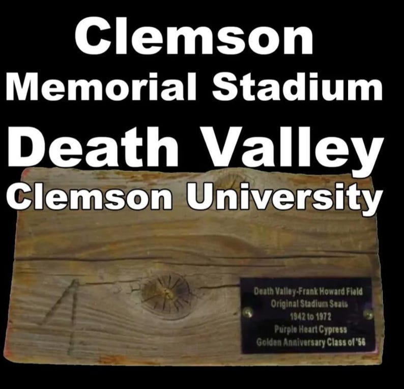 May include: A weathered wooden plaque with the text "Clemson Memorial Stadium Death Valley Clemson University." A smaller plaque reads "Death Valley-Frank Howard Field Original Stadium Seats 1942 to 1972." The wood has visible grain and knots.