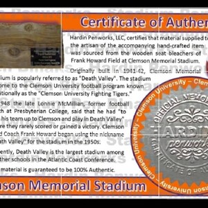 May include: Certificate of Authenticity for a Clemson Memorial Stadium item. The orange and white certificate includes text, a football, and a wooden section. The text mentions the stadium's history and the "Death Valley" nickname.