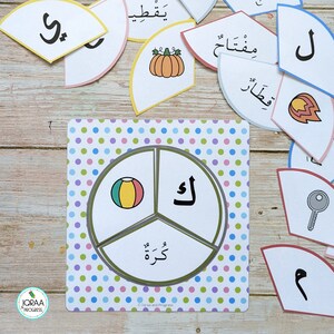 May include: A colorful, polka-dotted board game with a circular game board divided into three sections. The sections are labeled with the Arabic letters "la", "ka", and "wa".  A picture of a ball is in the "la" section.