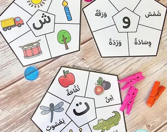 Peut inclure: Trois cartes éducatives pentagonales présentant des lettres et des chiffres arabes, chacune divisée en cinq sections avec des illustrations colorées d'objets comme un soleil, un camion, un tambour, un arbre, une bougie, une pomme, une figue, un crocodile, une couronne et une libellule.