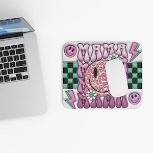 May include: A rectangular mousepad with a colorful design. The design includes the word "MAMA" in pink, a smiley face, lightning bolts, and a checkerboard pattern in green and black. A white computer mouse is on the mousepad.