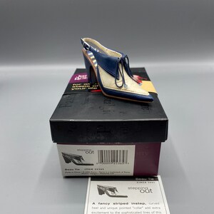 Peut inclure: Une figurine de chaussure slingback bleu marine et crème avec un bout pointu, un devant à lacets et une doublure rayée. La chaussure repose sur une boîte noire étiquetée Just The Right Shoe, accompagnée d'une carte descriptive intitulée Beau Tie.