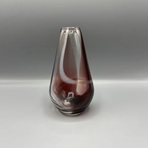 Könnte beinhalten: Eine kleine, klare Glasvase in Tropfenform. Die Vase hat ein wirbelndes Muster aus weißem und dunkelviolettem Glas.