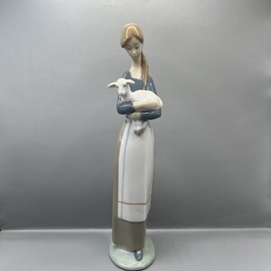 May include: A porcelain figurine of a woman in a blue dress and white apron holding a white lamb in her arms.