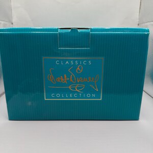 May include: A teal-colored box with a gold-colored rectangular label. The label features the words "CLASSICS" at the top, a signature, and the word "COLLECTION" at the bottom. The box is likely for a collectible item.