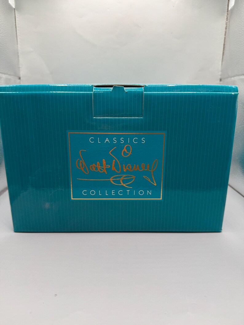 May include: A teal-colored box with a gold-colored rectangular label. The label features the words "CLASSICS" at the top, a signature, and the word "COLLECTION" at the bottom. The box is likely for a collectible item.