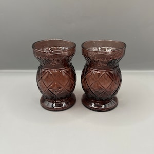 Puede incluir: Dos pequeños jarrones de vidrio transparente con un patrón de diamante y un tinte morado. Los jarrones están vacíos.