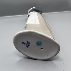 May include: The bottom of a porcelain figurine with a blue and white Lladro logo, the number 45, and the number 205. The figurine is white with a beige and gray dress.