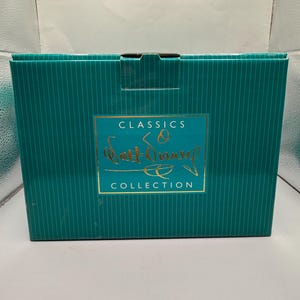 Peut inclure: Une bo&icirc;te turquoise &agrave; rayures verticales avec une &eacute;tiquette dor&eacute;e. L'&eacute;tiquette indique "CLASSICS" au-dessus de "Walt Disney" en cursive, et "COLLECTION" en dessous. La bo&icirc;te est ferm&eacute;e et semble neuve.