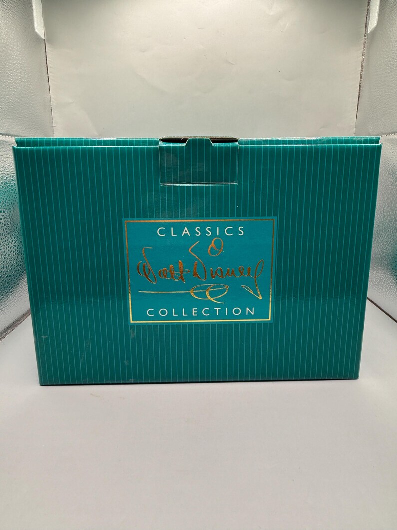 Peut inclure: Une bo&icirc;te turquoise &agrave; rayures verticales avec une &eacute;tiquette dor&eacute;e. L'&eacute;tiquette indique "CLASSICS" au-dessus de "Walt Disney" en cursive, et "COLLECTION" en dessous. La bo&icirc;te est ferm&eacute;e et semble neuve.