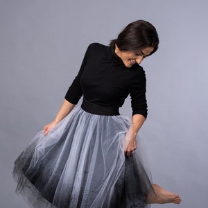 Könnte beinhalten: Eine Frau trägt ein schwarzes Rollkragen-Shirt und einen weißen und schwarzen Tüllrock. Der Rock hat einen Farbverlauf, der von Weiß zu Schwarz übergeht.