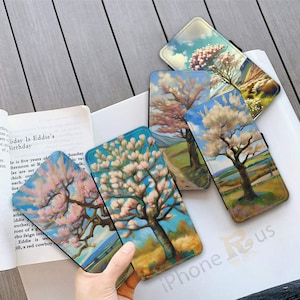 May include: Several phone cases with landscape art of flowering trees. Each case shows a different tree with pink or white blossoms against a blue sky, in a painted style. The cases are open.