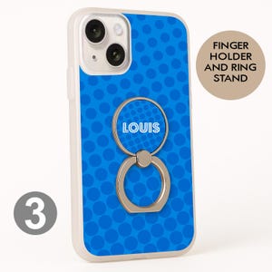 May include: A clear phone case with a blue polka dot design and a silver finger holder ring stand. The ring stand has the name "LOUIS" in white. The phone case has a camera and flash.