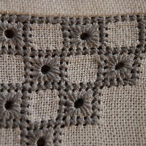 Puede incluir: Primer plano de una tela beige con un patrón bordado gris de cuadrados repetidos con un diseño floral en cada cuadrado.