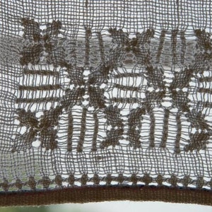 May include: A close-up of a white crocheted lace curtain with a delicate floral pattern. The lace is woven in a grid pattern with small holes throughout.