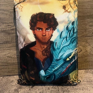 Könnte beinhalten: Eine Reißverschlusstasche mit einem farbenfrohen Design, das einen jungen Mann mit dunklen Haaren und einen blauen Drachen zeigt. Der Hintergrund ist ein gelbes und goldenes Wirbelmuster.