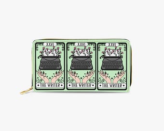 Könnte beinhalten: Eine mintgrüne Geldbörse mit goldenem Reißverschluss zeigt ein Tarotkarten-Design. Das Design umfasst eine schwarze Schreibmaschine mit Blumen, Händen und dem Text "THE WRITER". Die Geldbörse hat einen schwarzen Rand und die Nummer "XXVI".