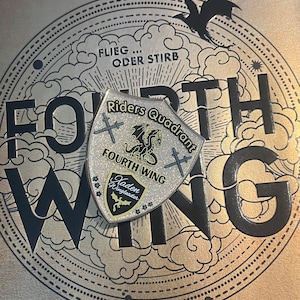 May include: A silver and black shield-shaped pin with a dragon and the text "Riders Quadrant Fourth Wing" and "Kaden Wingleader".