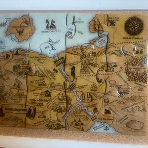 Può includere: Una mappa in stile vintage con un design fantasioso che presenta un drago di libro, un mare di sporcizia e una bussola morale. La mappa è divisa in sezioni con nomi come "Book Beaver Plateau", "The One Bed Inn" e "OTP Peaks".