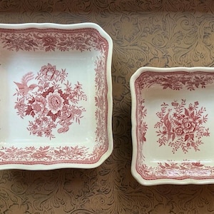 May include: Two square ceramic bowls with scalloped edges, featuring a cream-colored base and a detailed red floral pattern. The design includes central flower clusters and birds, with a decorative border along the inner rim of each bowl.