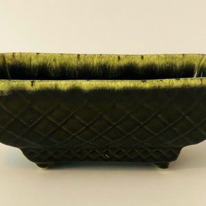 May include: A green ceramic planter with a diamond pattern and a yellow glaze. The planter has a rectangular shape with rounded edges and four small feet.