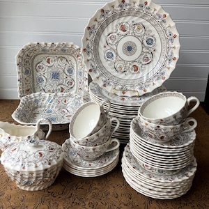 May include: A complete vintage porcelain dinnerware set with a detailed floral and scroll design in shades of white, brown, blue, and red. The set includes plates, cups, saucers, a serving dish, and a covered sugar bowl.