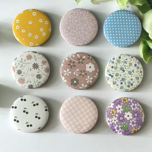 May include: Nine round decorative buttons with floral, polka dot, and gingham patterns. The buttons feature a variety of colors, including yellow, pink, blue, and purple. The buttons are arranged in a grid.