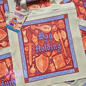 Pode incluir: Uma bolsa de lona bege com um design azul e vermelho. A bolsa apresenta uma ilustração caprichosa de uma variedade de itens de fantasia, incluindo uma espada, um escudo, uma lanterna, um livro e um alaúde. O texto "Bag of Holding" está impresso em uma fonte estilizada na bolsa.