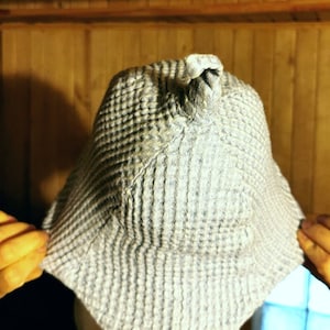 Può includere: Un cappello con cappuccio in maglia a nido d'ape grigio con una punta a punta. Il cappello è tenuto dalle mani di una persona.