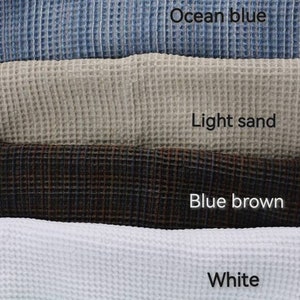 Pode incluir: Uma pilha de toalhas de tecido waffle em v&aacute;rias cores, incluindo roxo oceano, verde oceano, azul oceano, areia clara, marrom azul, branco, menta e azul claro.