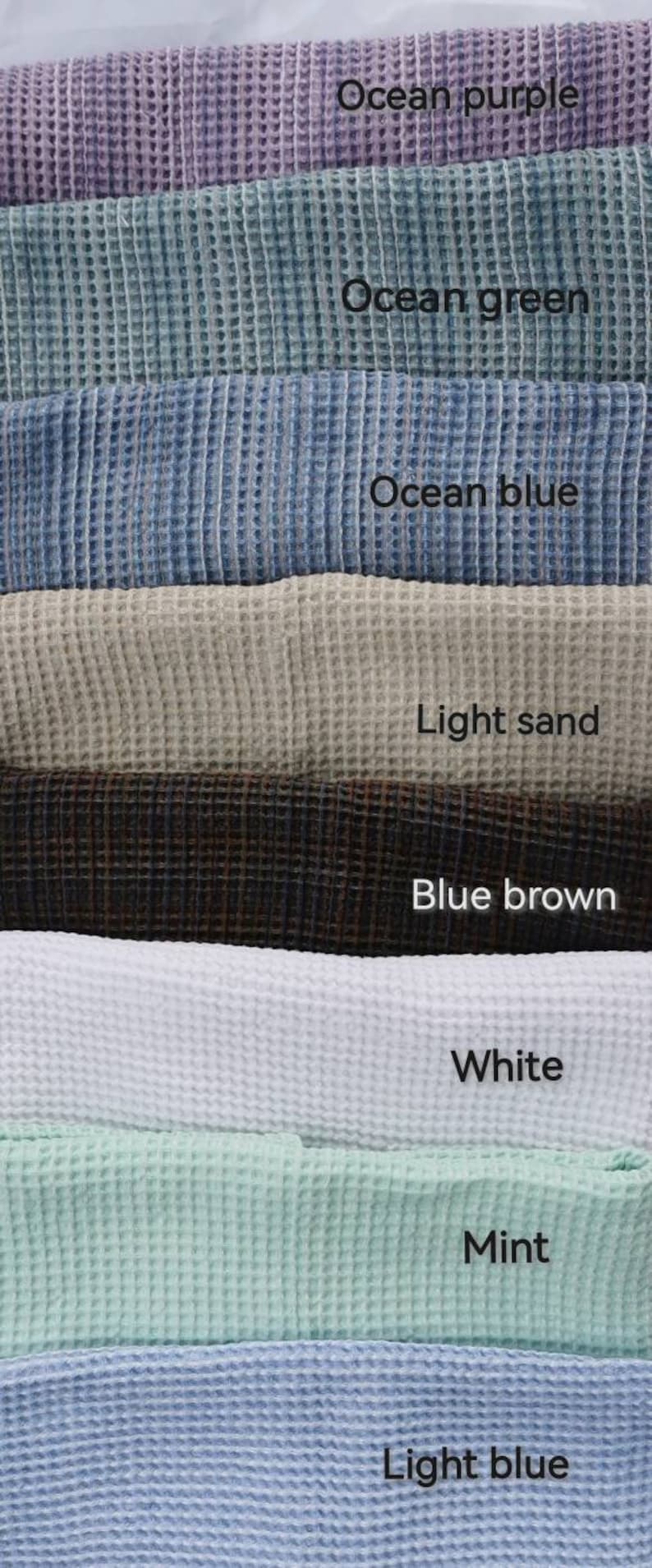 Pode incluir: Uma pilha de toalhas de tecido waffle em v&aacute;rias cores, incluindo roxo oceano, verde oceano, azul oceano, areia clara, marrom azul, branco, menta e azul claro.