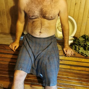May include: A man wearing a blue and gray checkered wrap skirt in a wooden sauna.