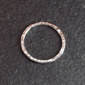 Op de afbeelding: Een eenvoudige zilveren ring met een gehamerde textuur. De ring is rond en heeft een gladde, gepolijste afwerking.