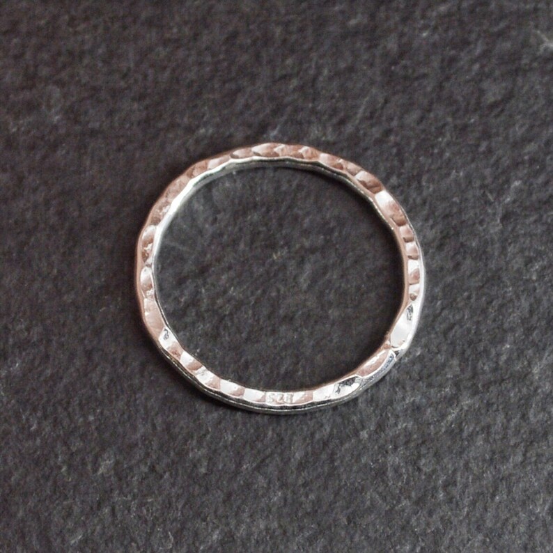Op de afbeelding: Een eenvoudige zilveren ring met een gehamerde textuur. De ring is rond en heeft een gladde, gepolijste afwerking.