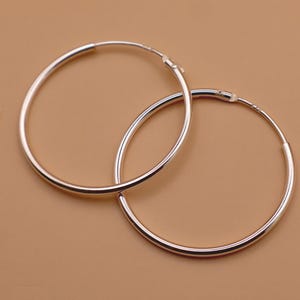 May include: A pair of polished silver hoop earrings with a circular design. The earrings feature a thin, smooth metallic band that forms a complete circle, with a small hinged clasp mechanism visible at the top of each hoop for secure closure.