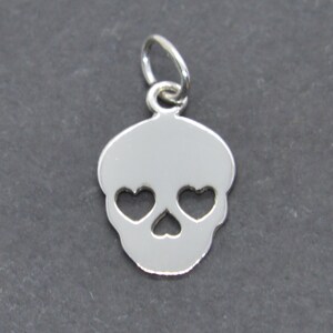 May include: Silver charm in the shape of a skull with heart-shaped eyes.