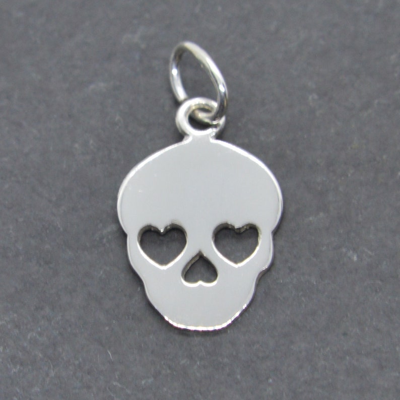 May include: Silver charm in the shape of a skull with heart-shaped eyes.