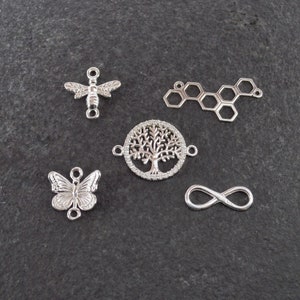 Op de afbeelding: Vijf zilveren bedels: een bij, een vlinder, een levensboom, een honingraat en een oneindigheidssymbool. Deze bedels zijn perfect voor het maken van sieraden.