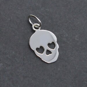 May include: Silver charm in the shape of a skull with heart-shaped eye cutouts.
