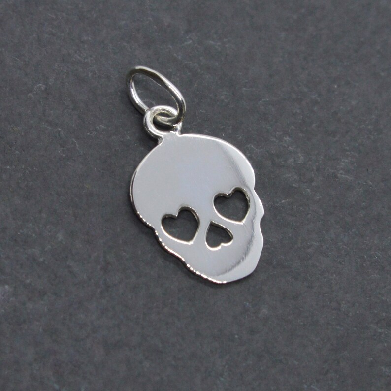 May include: Silver charm in the shape of a skull with heart-shaped eye cutouts.