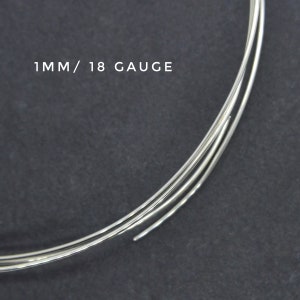 May include: Close-up of three strands of silver wire, each 1 mm thick, or 18 gauge. The wire is coiled and resting on a dark gray surface.