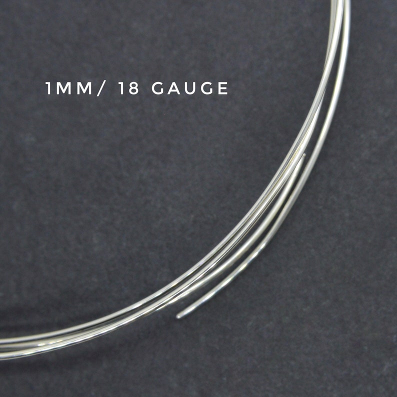 May include: Close-up of three strands of silver wire, each 1 mm thick, or 18 gauge. The wire is coiled and resting on a dark gray surface.