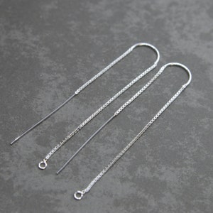 May include: Three silver chain earrings with a loop at the top and a small circle at the bottom. The chains are different lengths.