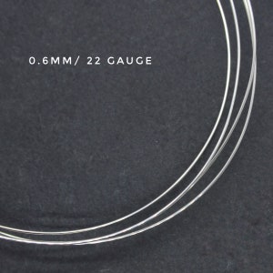 May include: Close-up of three strands of silver wire, 0.6mm in diameter, or 22 gauge. The wire is coiled and lying on a dark gray surface.