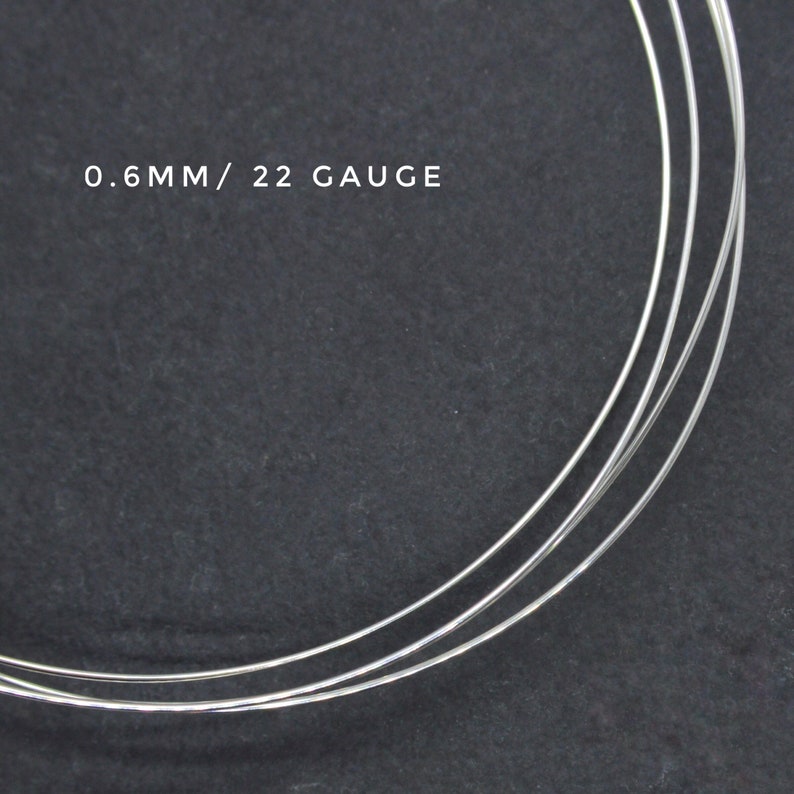 May include: Close-up of three strands of silver wire, 0.6mm in diameter, or 22 gauge. The wire is coiled and lying on a dark gray surface.