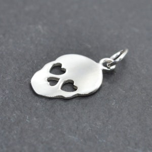 May include: Silver charm in the shape of a skull with heart-shaped eye cutouts.