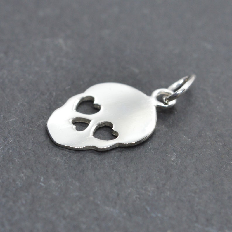 May include: Silver charm in the shape of a skull with heart-shaped eye cutouts.