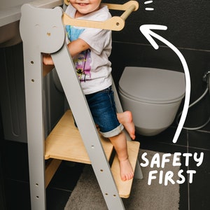 Könnte beinhalten: Ein grauer und naturbelassener Holztritt mit einem Bärengesicht-Design an der Seite. Der Hocker hat eine kleine Plattform und einen Griff. Der Text "SAFETY FIRST" ist auf dem Bild geschrieben.